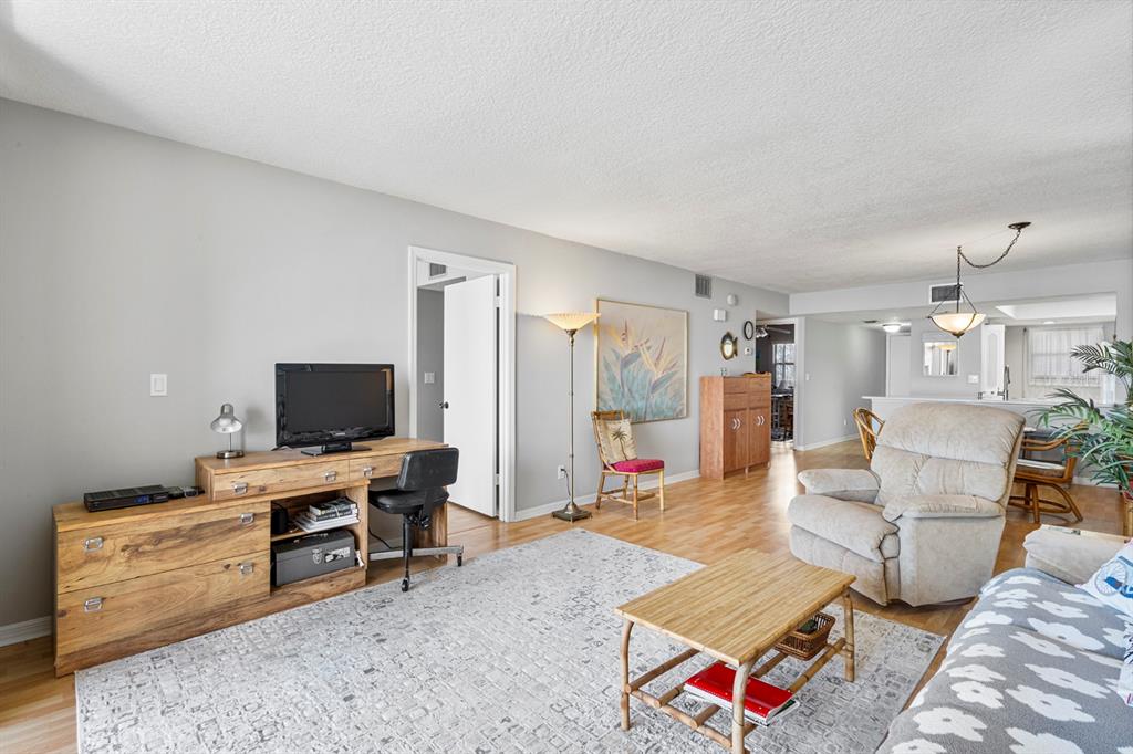 A living room features light gray walls, wood flooring, a desk, and a beige recliner — 1890 N ATLANTIC AVENUE UNIT A404, COCOA BEACH, FL