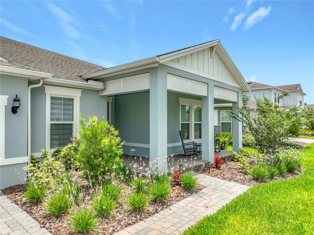A light blue house features a covered front porch, a paver walkway, and landscaped gardens — 10774 PAHOKEE BEACH PLACE, ORLANDO, FL