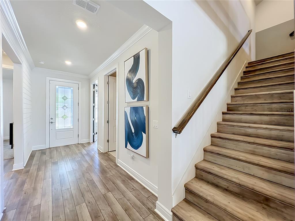 A bright entryway features wood-look tile flooring, a staircase with a wooden railing, and artwork — 10774 PAHOKEE BEACH PLACE, ORLANDO, FL