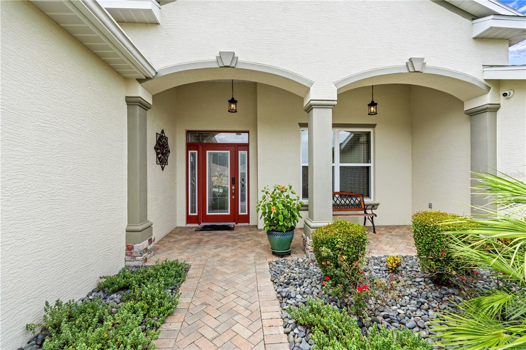 A paved walkway leads to the covered front porch of a house with a red door — 4419 BENT CREEK LANE, LEESBURG, FL