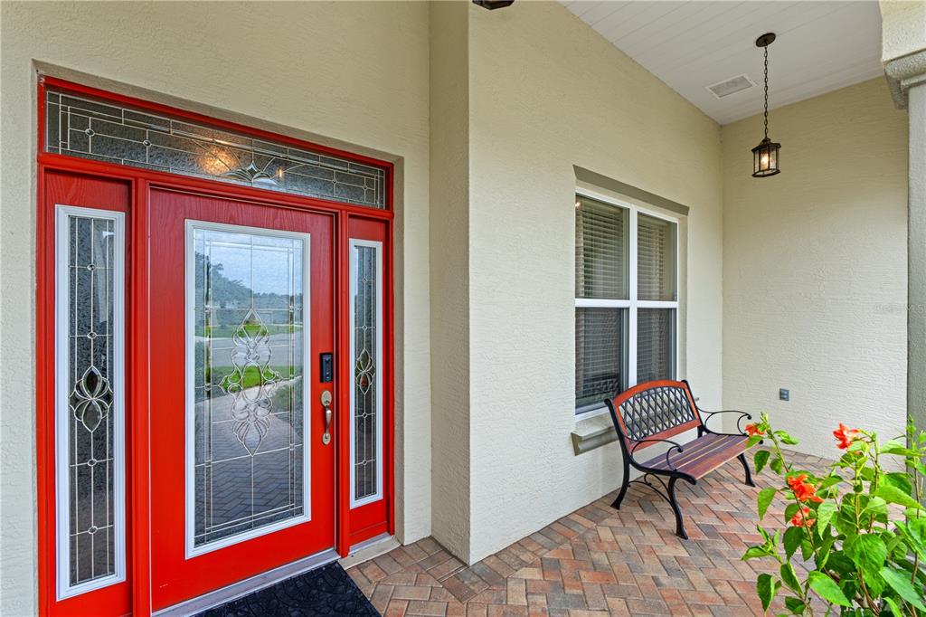 A red front door with glass inserts sits on a covered porch with a bench — 4419 BENT CREEK LANE, LEESBURG, FL