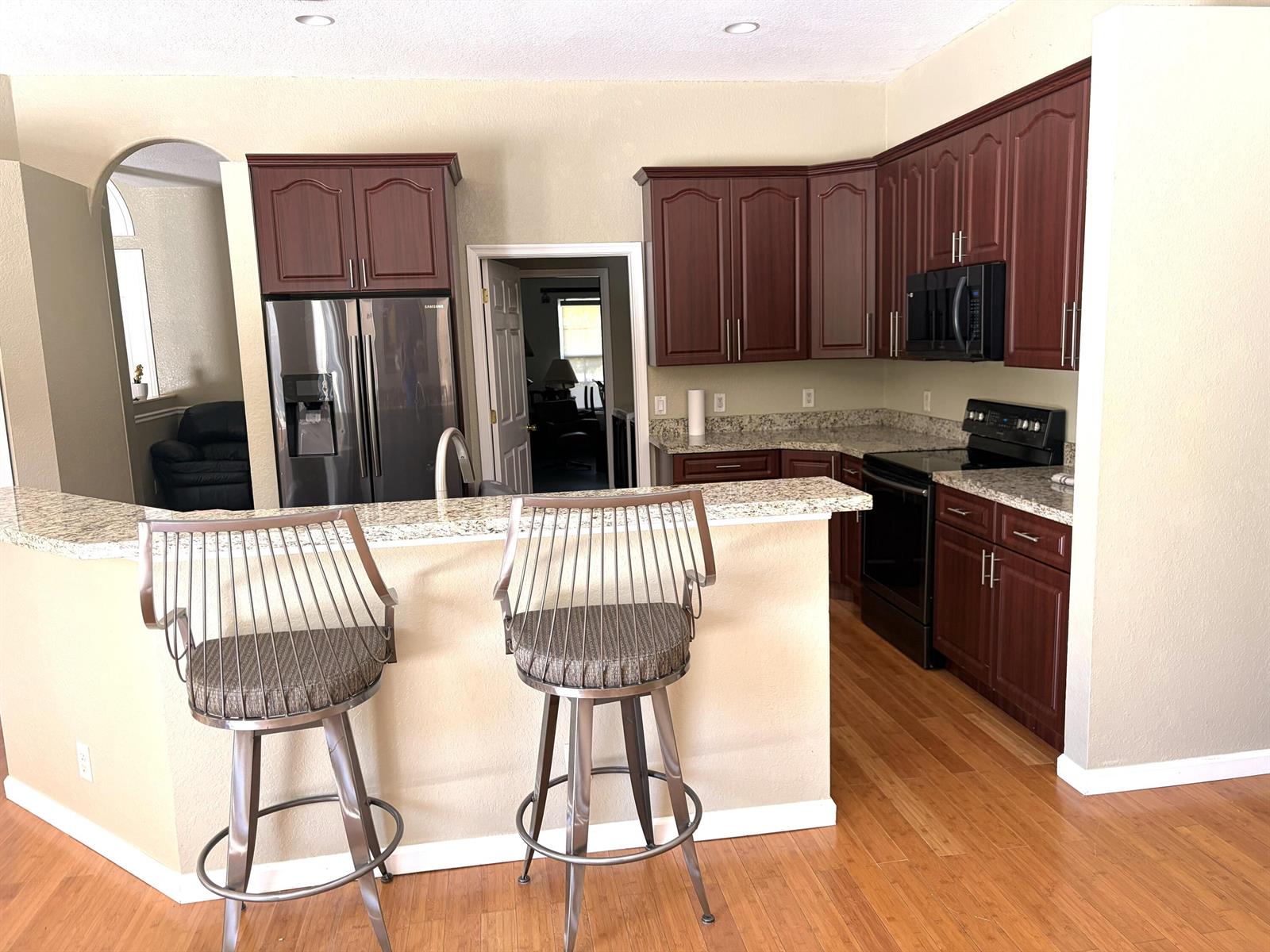A kitchen features dark wood cabinets, granite countertops, stainless steel appliances, and two bar stools — 7611 N 140th Ave Avenue N, FL 33412, FL