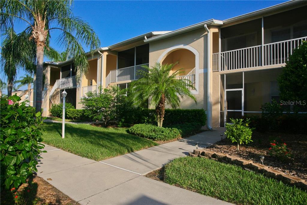 A two-story apartment building exterior features screened balconies, a palm tree, and a concrete walkway — 5270 HYLAND HILLS AVENUE UNIT 1722, SARASOTA, FL