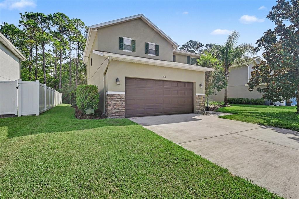 A two-story house with a brown garage door, stone accents, and a green lawn — 65 PERGOLA PLACE, ORMOND BEACH, FL