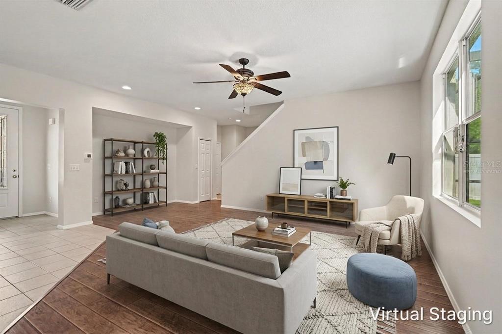 A living room with wood-look flooring, a grey sofa, a coffee table, and virtual staging — 65 PERGOLA PLACE, ORMOND BEACH, FL