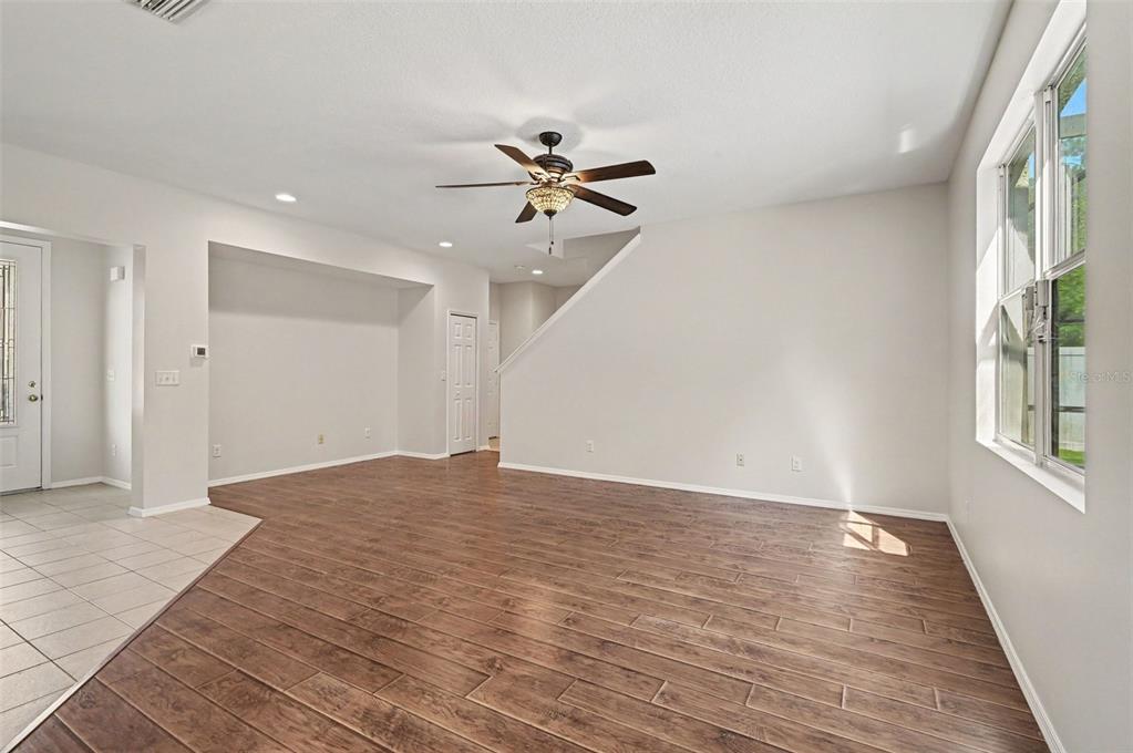An empty living room features wood-look tile flooring, a ceiling fan, and a staircase — 65 PERGOLA PLACE, ORMOND BEACH, FL