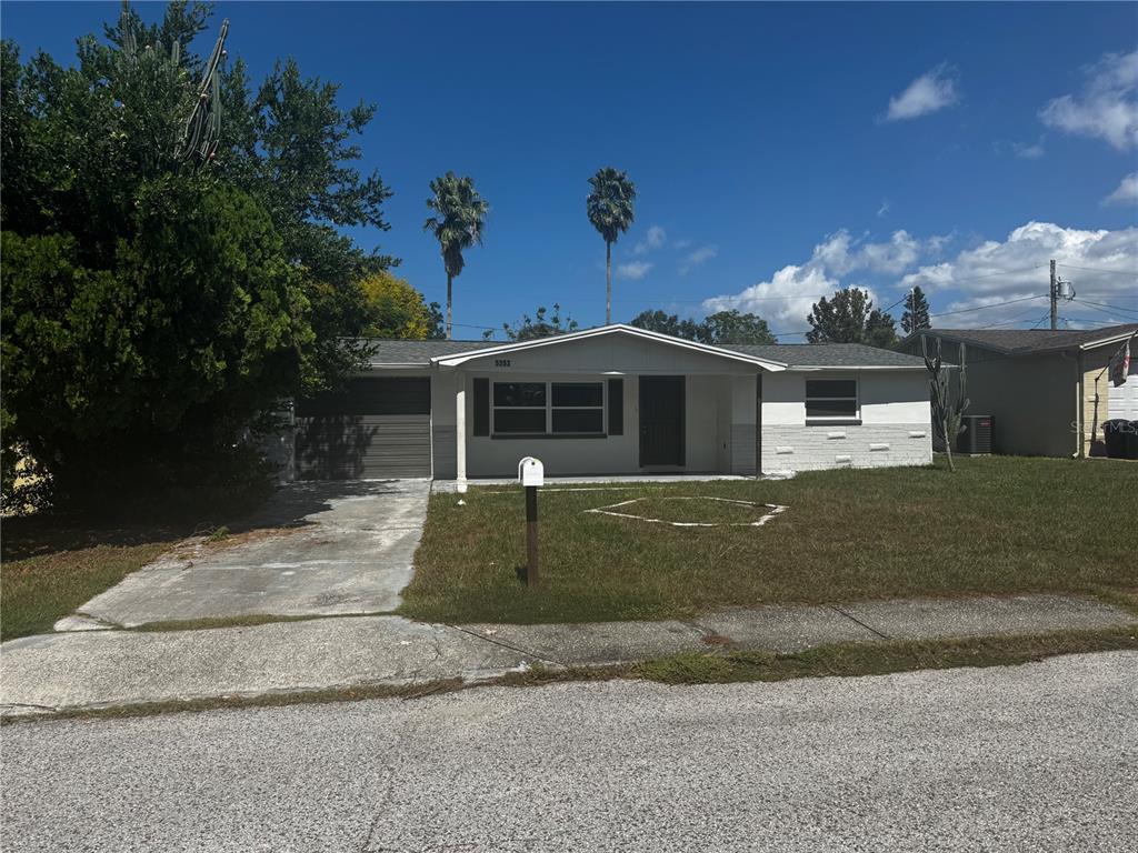 A single-story house with a white exterior, a garage, and a front lawn under blue skies — 5253 DEVRIES DRIVE, NEW PORT RICHEY, FL
