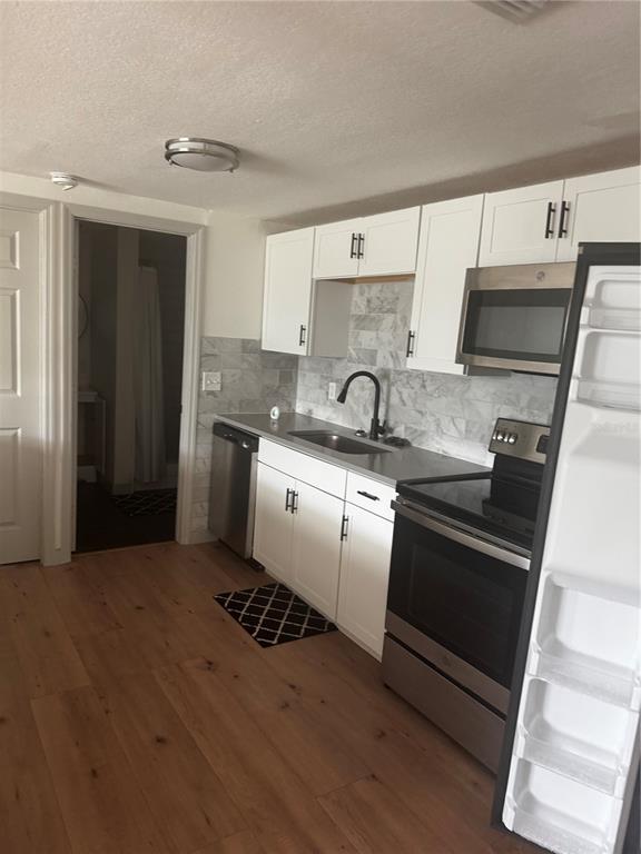A kitchen features white cabinets, stainless steel appliances, a marble backsplash, and wood-look flooring — 5253 DEVRIES DRIVE, NEW PORT RICHEY, FL