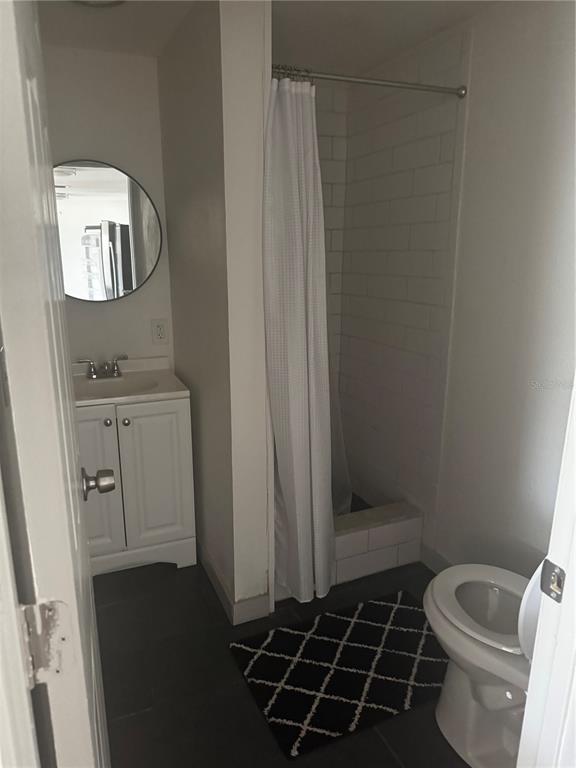 A small bathroom features a white vanity, a round mirror, and a tiled shower stall — 5253 DEVRIES DRIVE, NEW PORT RICHEY, FL