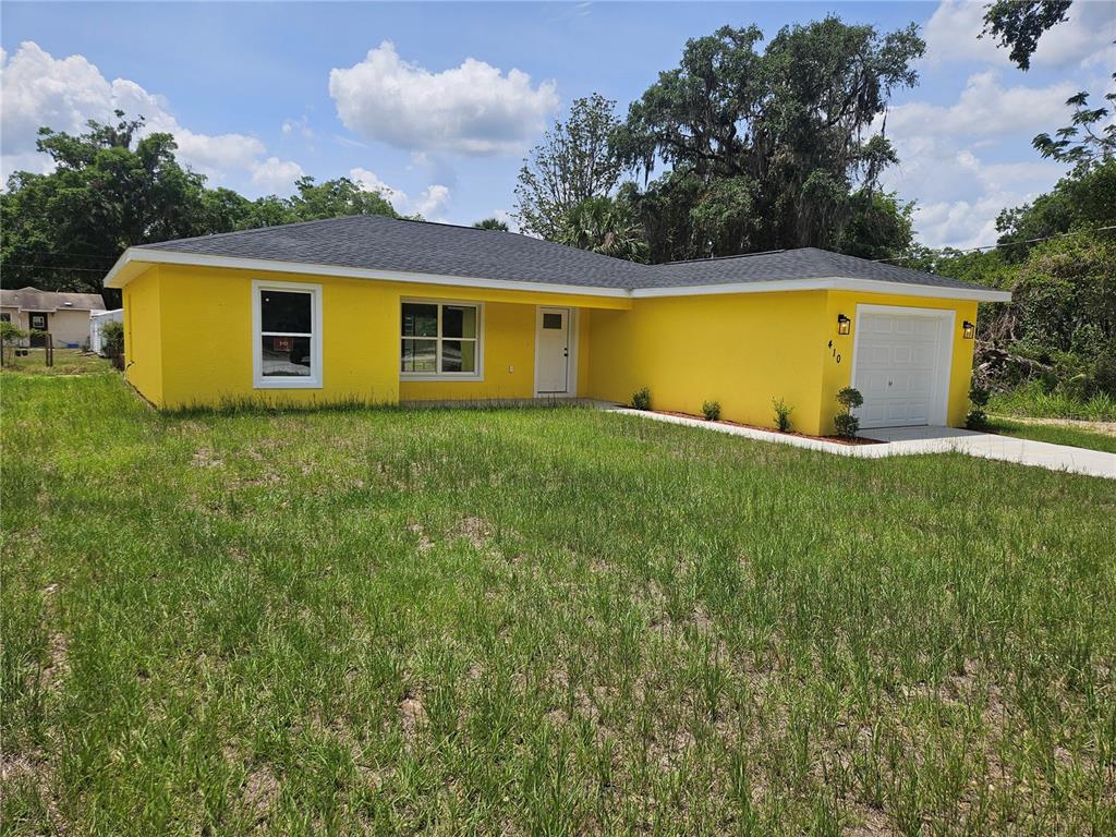 A bright yellow, single-story house with a dark roof and a one-car garage — 410 KILGORE STREET, WILDWOOD, FL