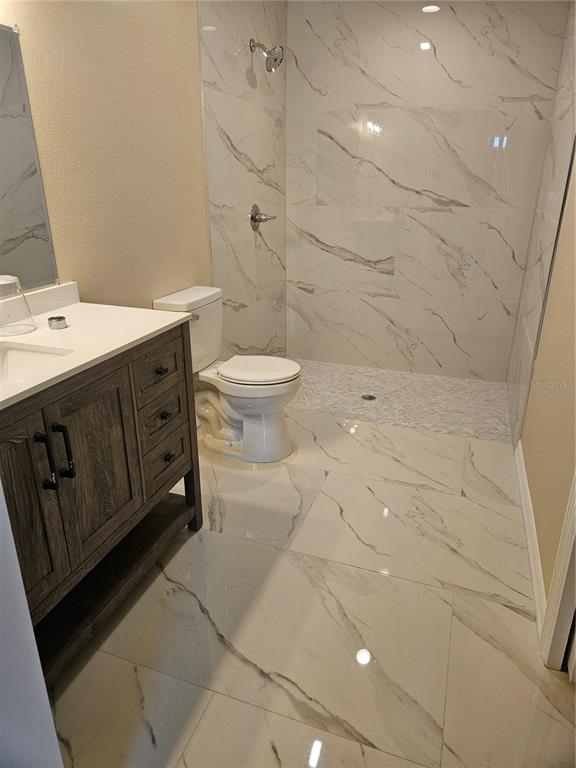 A bathroom features a wood vanity, a white toilet, and a walk-in marble-tiled shower — 410 KILGORE STREET, WILDWOOD, FL