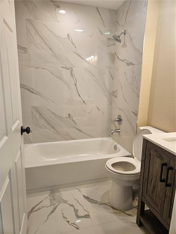 A bathroom features a white bathtub with marble-patterned tile walls and matching floor tiles — 410 KILGORE STREET, WILDWOOD, FL
