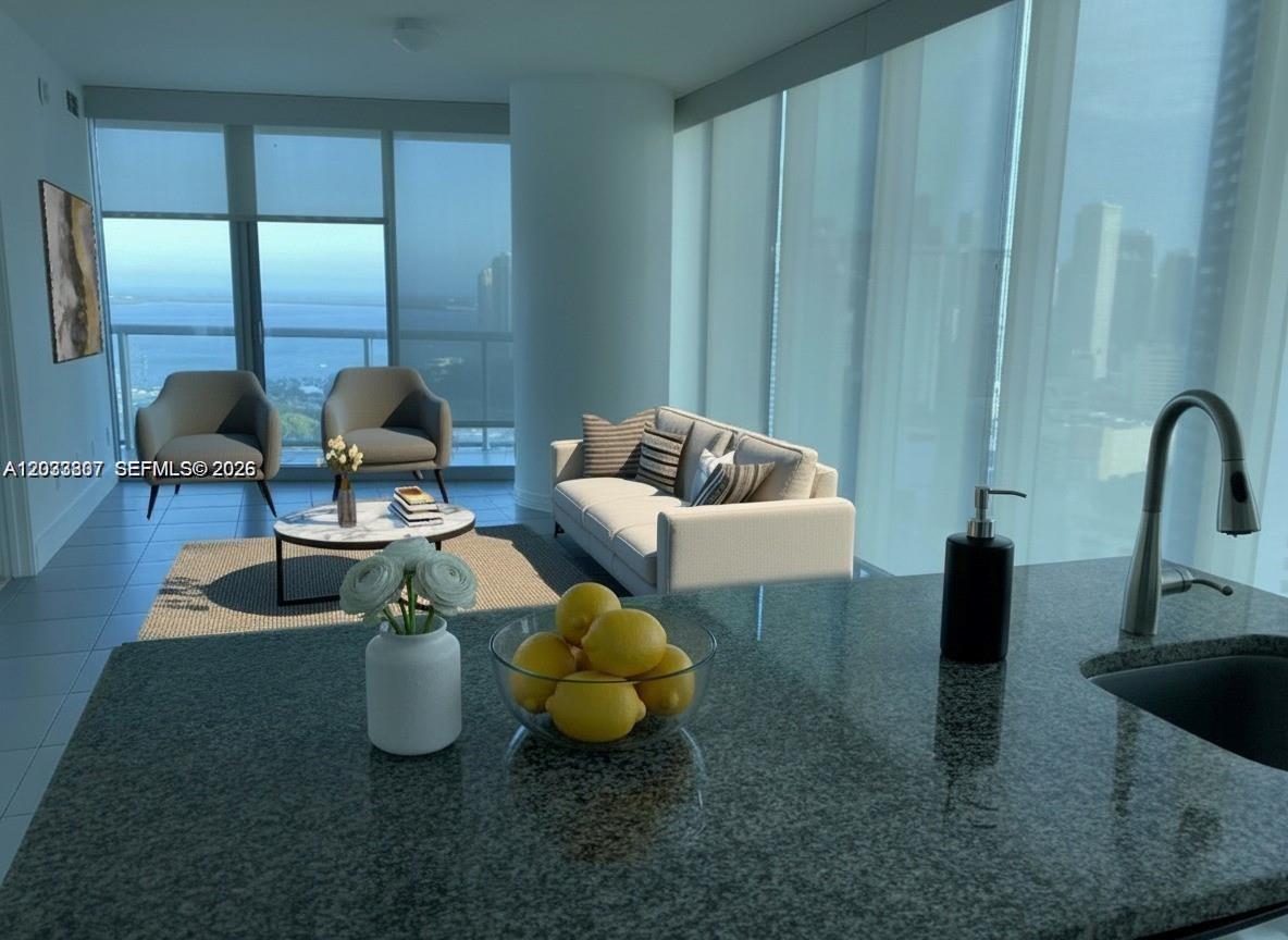 A kitchen island with lemons overlooks a living area with floor-to-ceiling windows and water views — 888 Biscayne Blvd # 3001, Miami FL 33132, MIAMI, FL