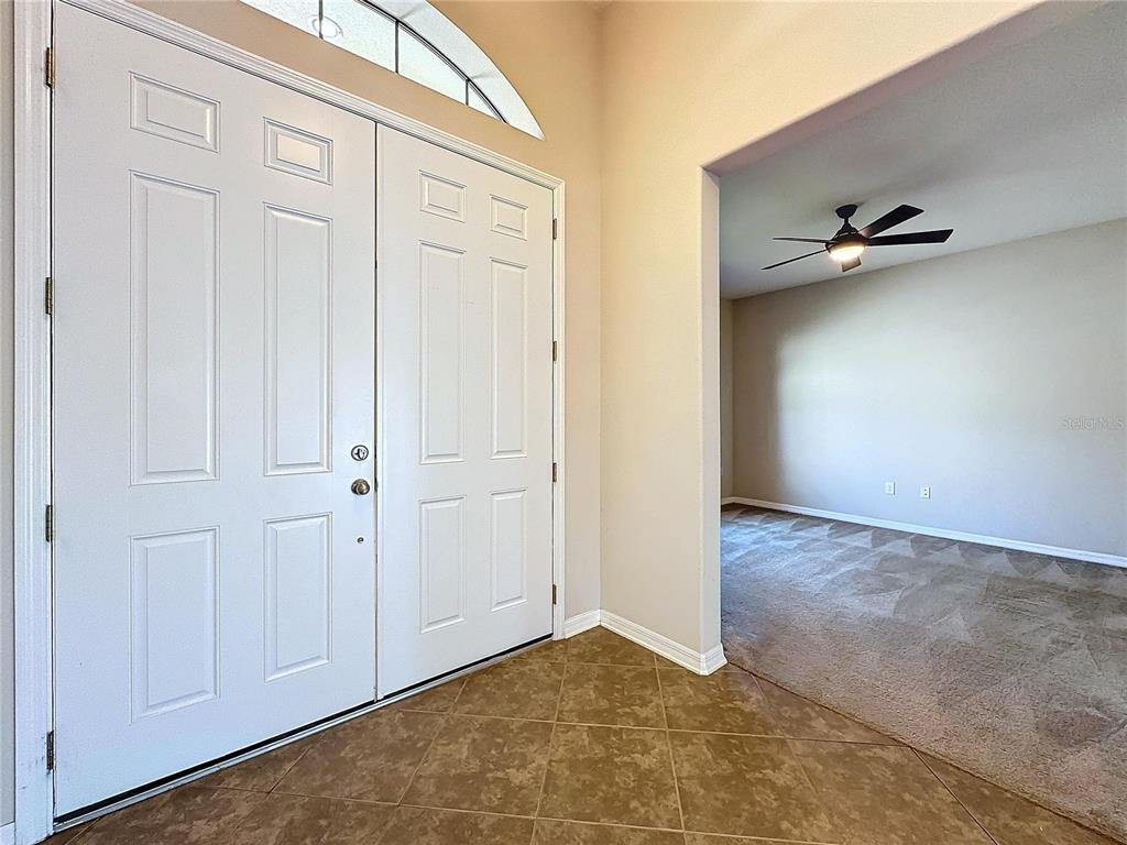An entryway with a double door and tile floor leads into a carpeted room — 5121 APPENINE LOOP W, ST CLOUD, FL