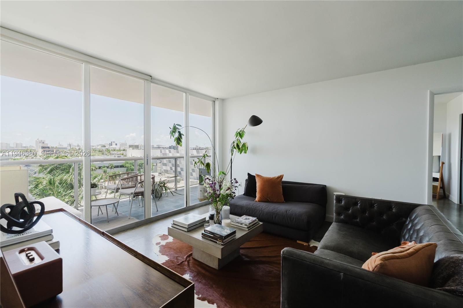 A modern living room features a dark sofa, a cowhide rug, and floor-to-ceiling balcony windows — 1900 Sunset Harbour Dr # 703, Miami Beach FL 33139, MIAMI BEACH, FL