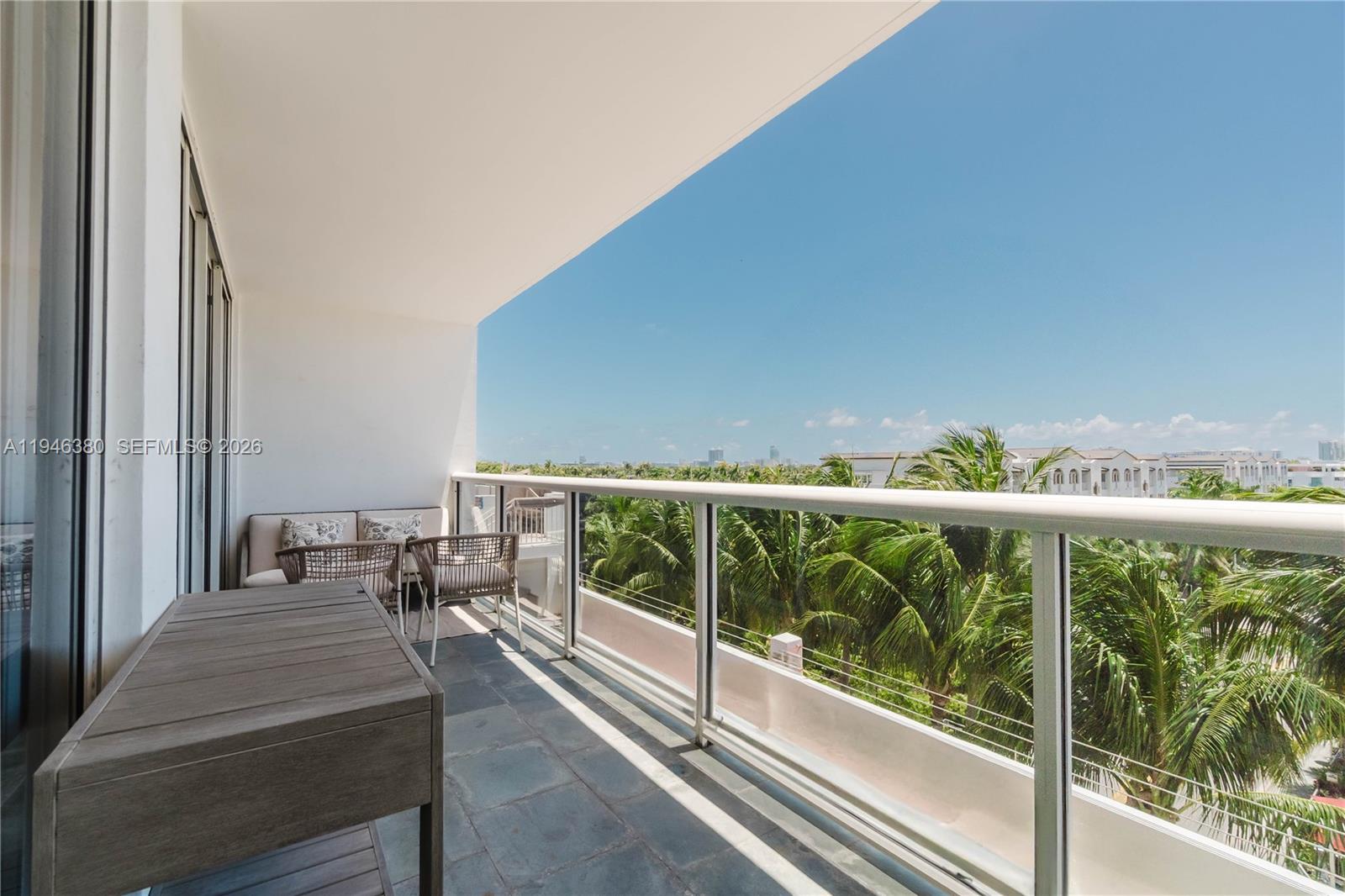 A balcony with a glass railing overlooks palm trees under a clear blue sky — 1900 Sunset Harbour Dr # 703, Miami Beach FL 33139, MIAMI BEACH, FL