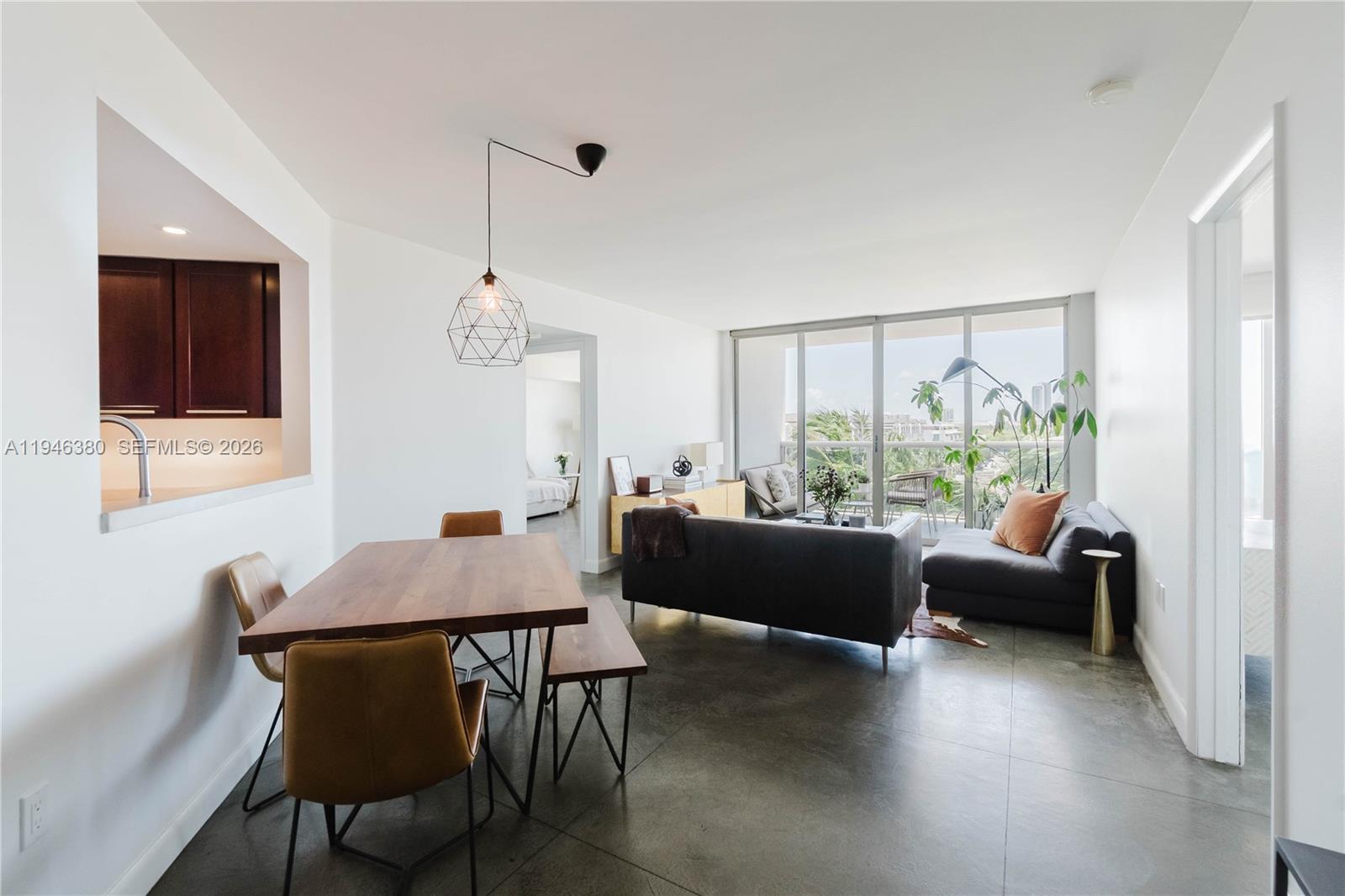 An open-concept living and dining area features concrete floors, a modern pendant light, and balcony — 1900 Sunset Harbour Dr # 703, Miami Beach FL 33139, MIAMI BEACH, FL