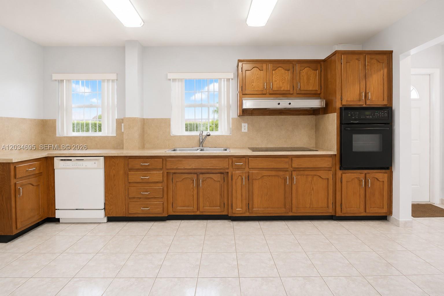 A kitchen with wood cabinets, a white dishwasher, a black wall oven, and tile flooring — 9120 SW 16th St, Miami FL 33165, MIAMI, FL