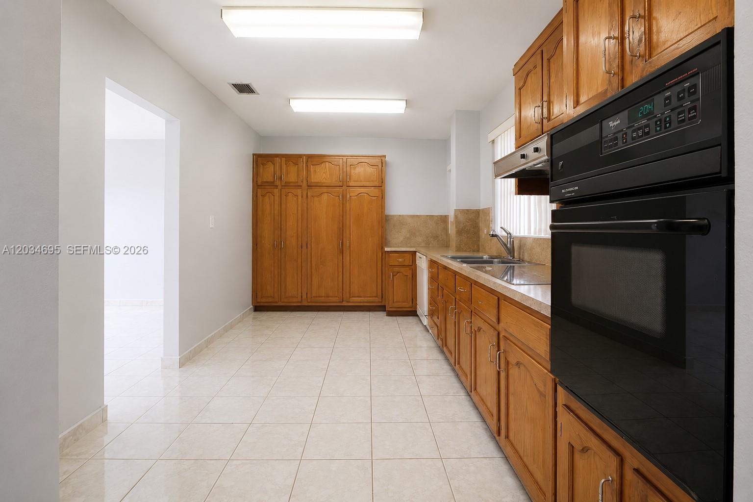 A kitchen features wood cabinets, a black wall oven, and light tile flooring — 9120 SW 16th St, Miami FL 33165, MIAMI, FL