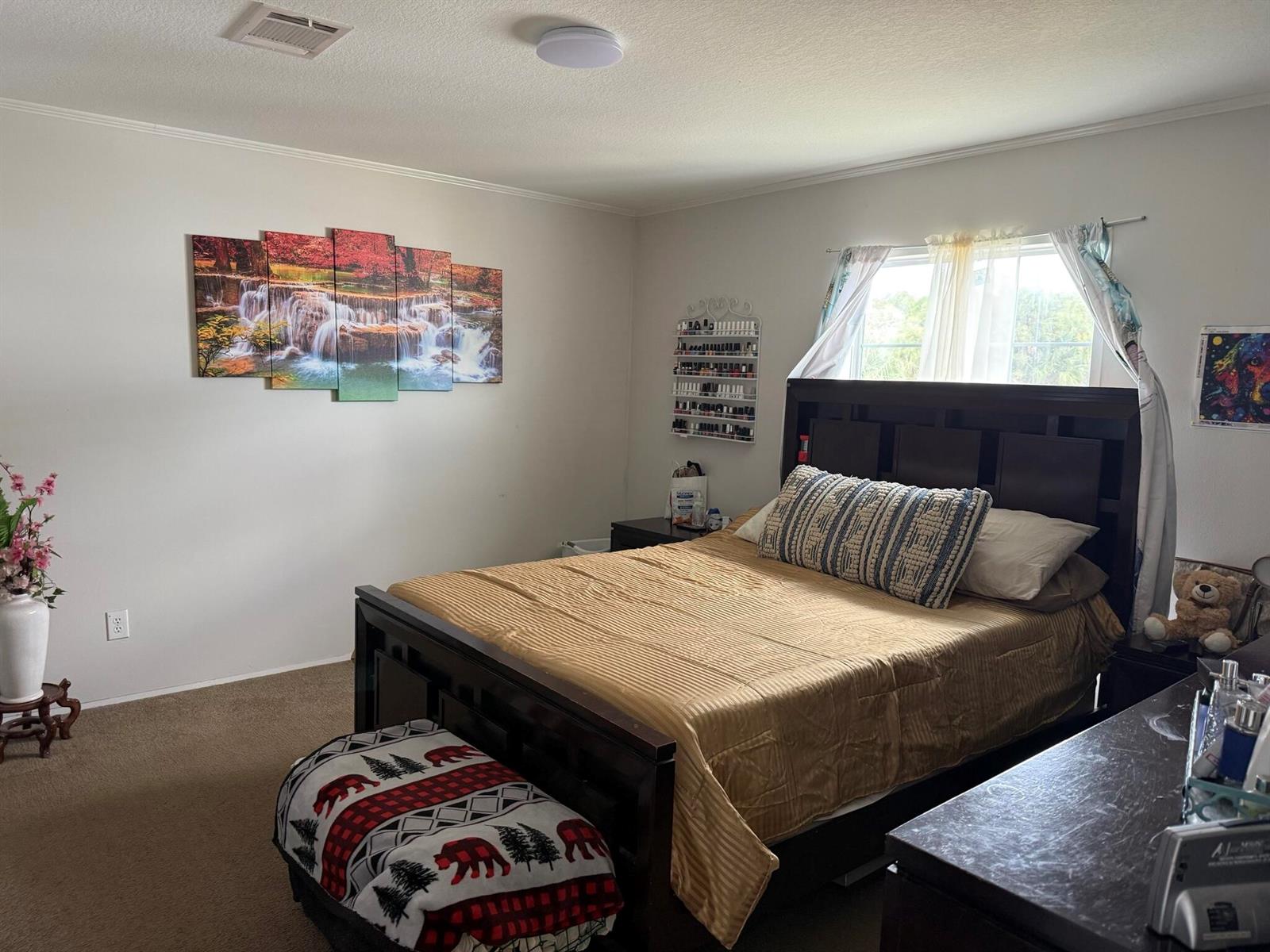 A bedroom features a dark wood bed frame, a gold bedspread, and a waterfall wall art — 15628 NW 310th Street, Okeechobee FL 34972, OKEECHOBEE, FL