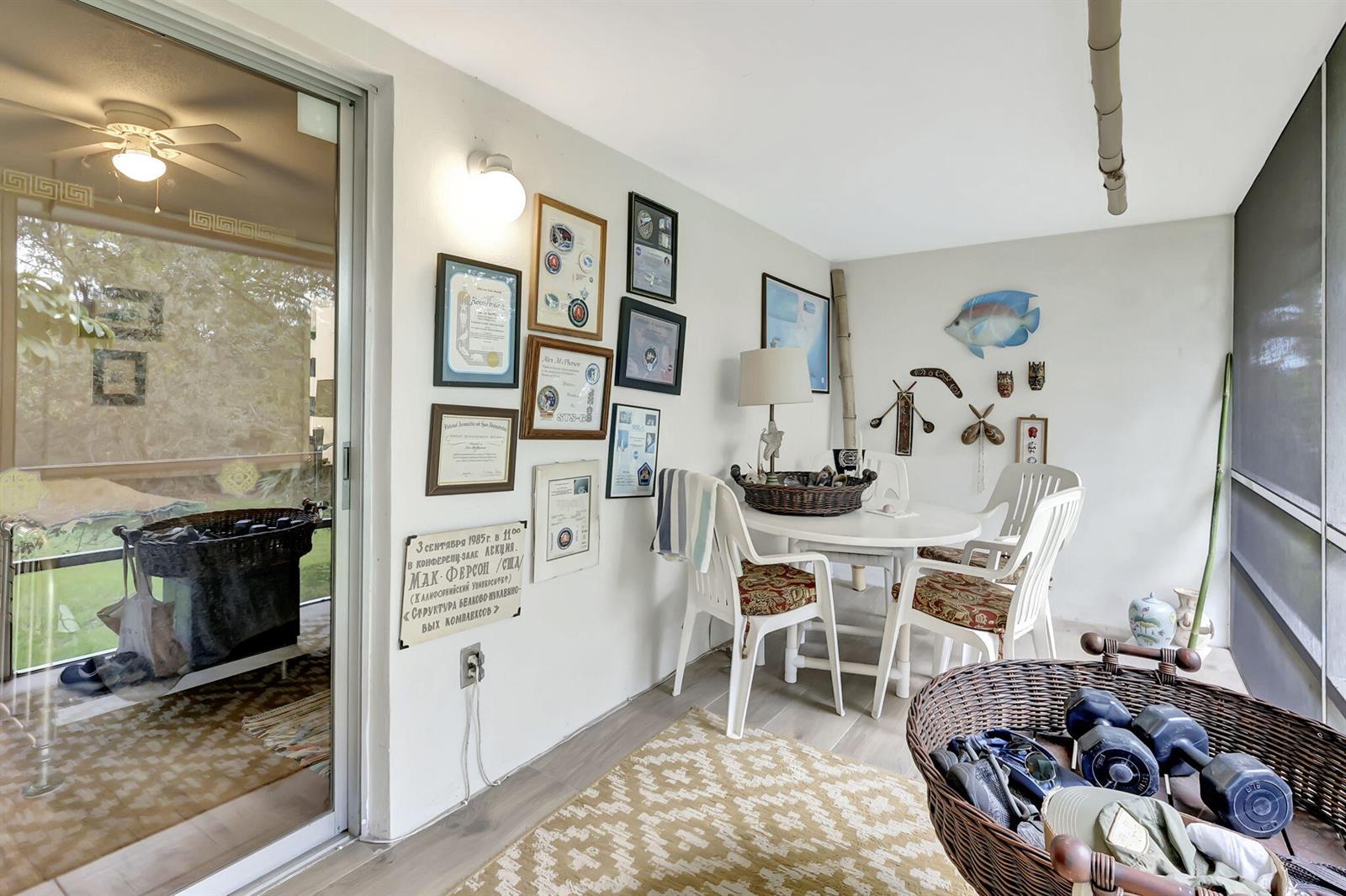 A sunroom features a dining set, wall-mounted certificates, and a wicker basket with weights — 2929 SE Ocean Boulevard # 7, Stuart FL 34996, STUART, FL