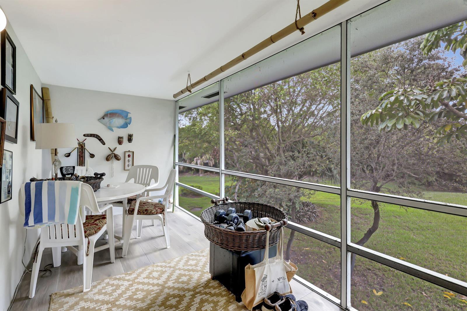 A sunroom features a dining set, a basket of weights, and large windows overlooking trees — 2929 SE Ocean Boulevard # 7, Stuart FL 34996, STUART, FL