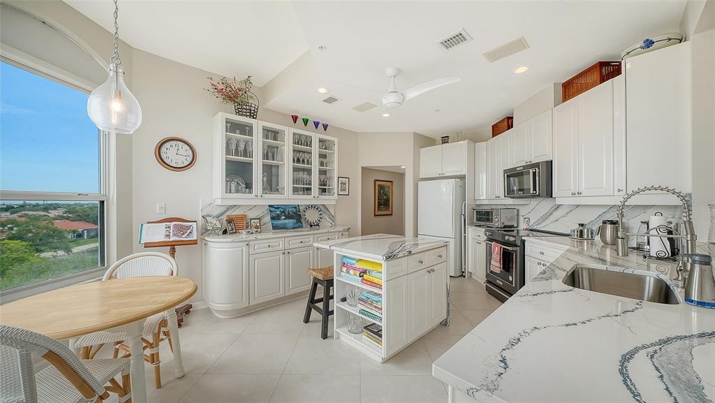 A bright kitchen features white cabinetry, marble-patterned countertops, a central island, and a dining area — 5420 EAGLES POINT CIRCLE UNIT 406, SARASOTA, FL