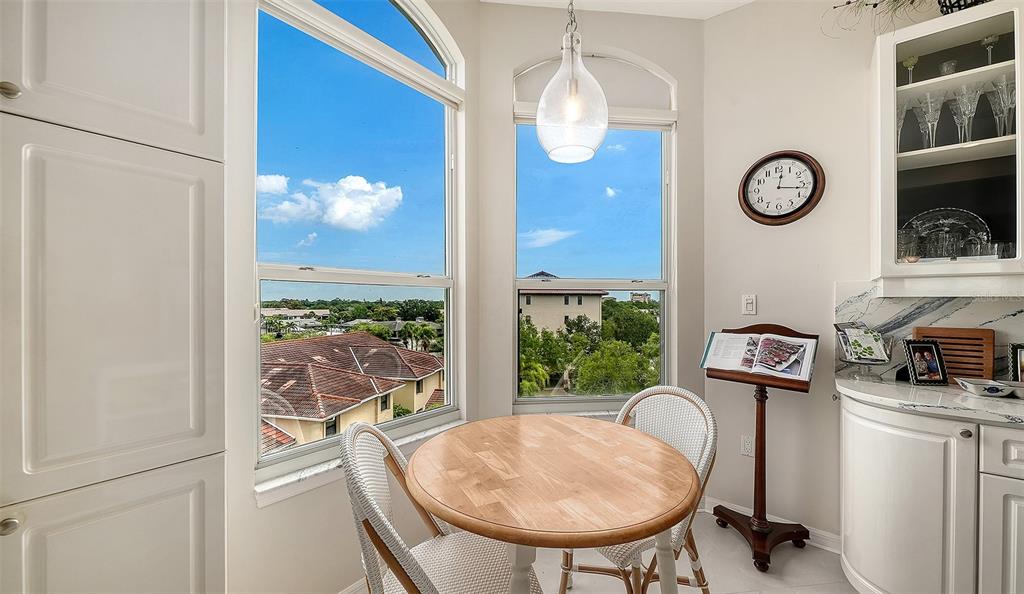 A breakfast nook features a round wooden table, two chairs, large windows, and a wall clock — 5420 EAGLES POINT CIRCLE UNIT 406, SARASOTA, FL