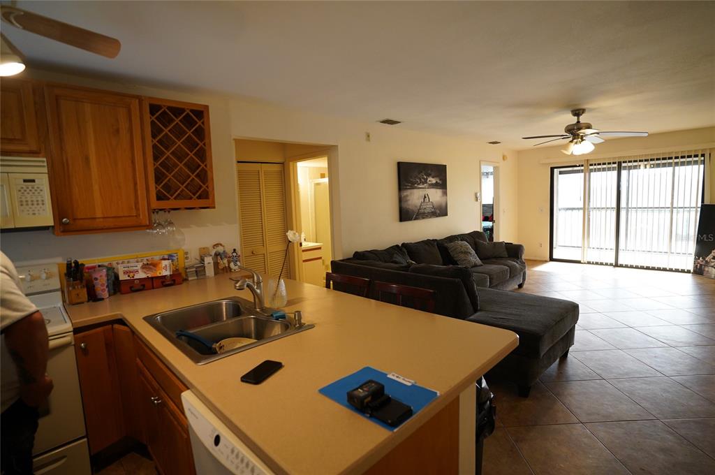 A kitchen with light countertops and wood cabinets overlooks an open-concept living room with tile — 26485 RAMPART BOULEVARD UNIT D21, PUNTA GORDA, FL