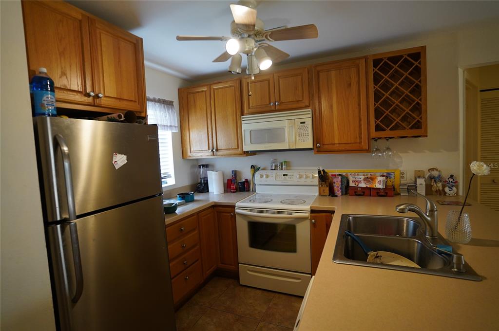 A kitchen features oak cabinets, stainless steel appliances, a white stove, and a double sink — 26485 RAMPART BOULEVARD UNIT D21, PUNTA GORDA, FL