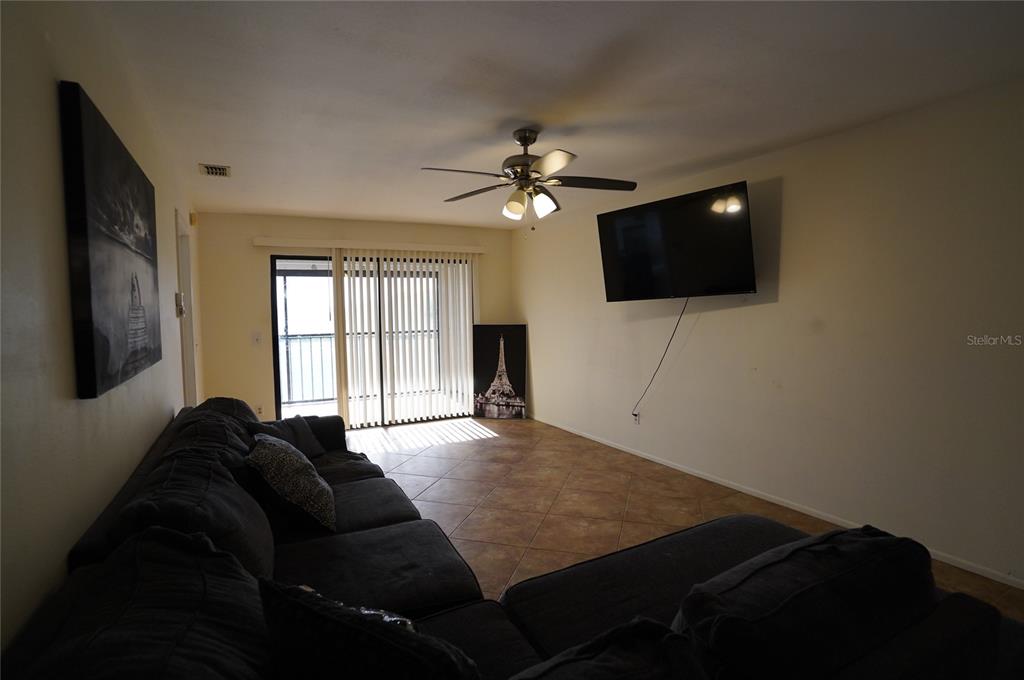 A living room features tile flooring, a ceiling fan, a wall-mounted television, and sliding glass doors — 26485 RAMPART BOULEVARD UNIT D21, PUNTA GORDA, FL