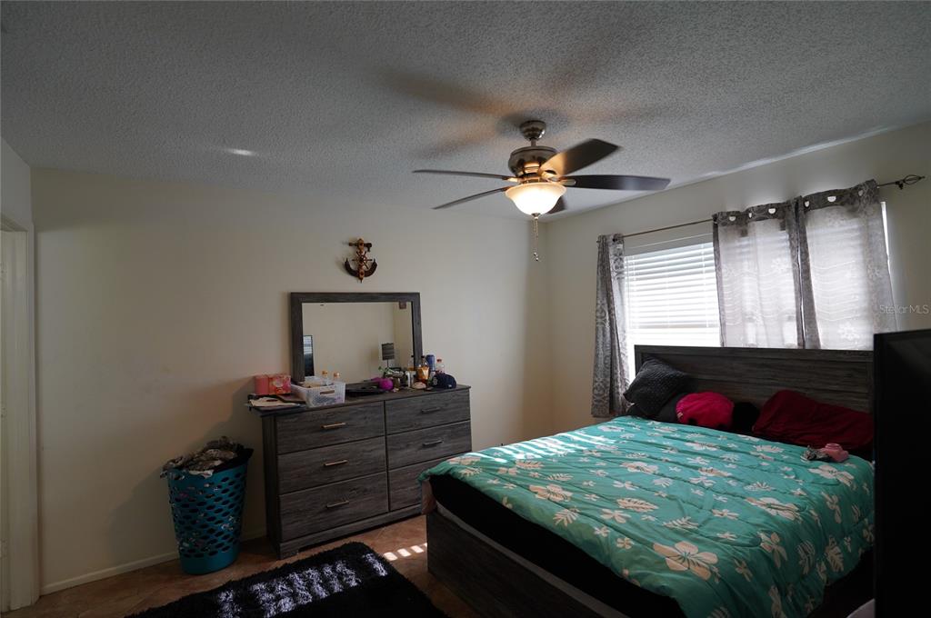 A bedroom features a bed with a floral comforter, a dresser with a mirror, and a fan — 26485 RAMPART BOULEVARD UNIT D21, PUNTA GORDA, FL