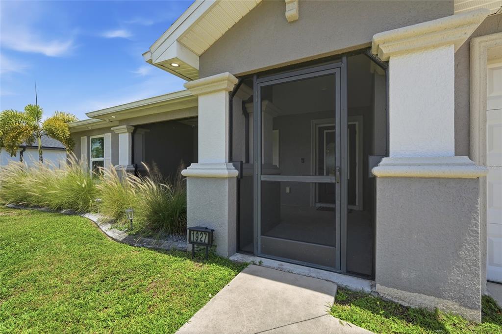 A gray house exterior features a screened front entryway and a house number sign — 1927 NE 33RD STREET, CAPE CORAL, FL