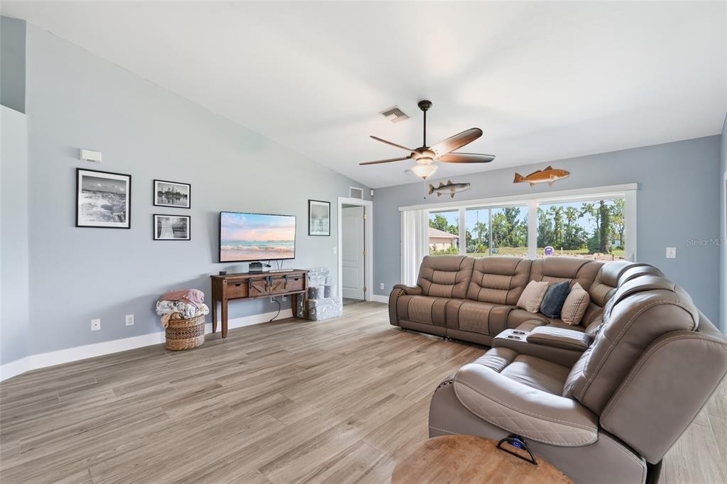 A living room features light blue walls, wood-look flooring, a sectional sofa, and a ceiling fan — 1927 NE 33RD STREET, CAPE CORAL, FL