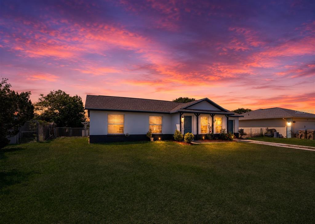 A single-story house with a white exterior and dark brick base under a sunset sky — 17 TROTTERS CIRCLE, KISSIMMEE, FL