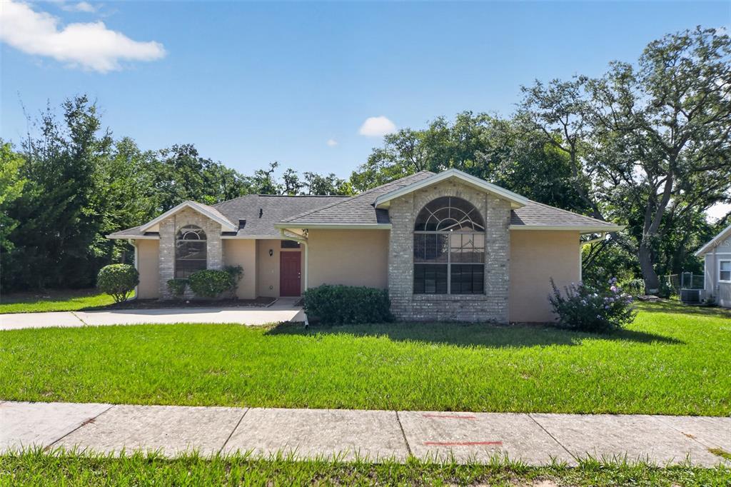 A single-story house with a tan stucco exterior, brick accents, and a red front door — 6348 SLEEPY HOLLOW DRIVE, ORLANDO, FL