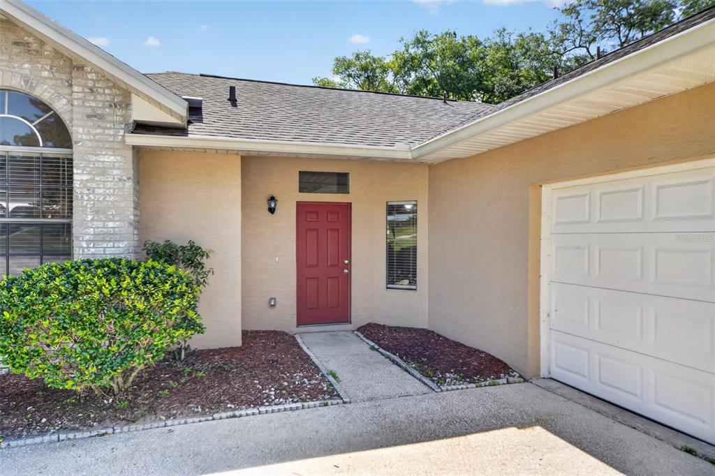 A tan house exterior features a red front door, a white garage door, and landscaping — 6348 SLEEPY HOLLOW DRIVE, ORLANDO, FL
