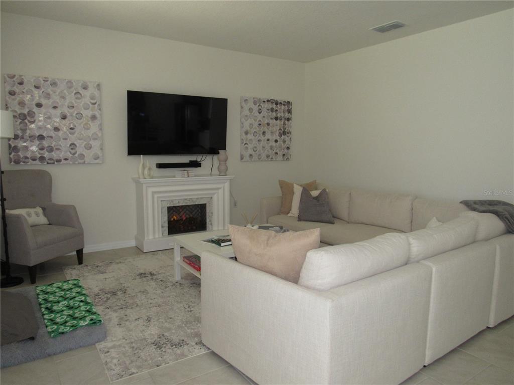 A living room features a white sectional sofa, a fireplace with a television, and artwork — 1739 RED ROCK ROAD, NEW SMYRNA BEACH, FL