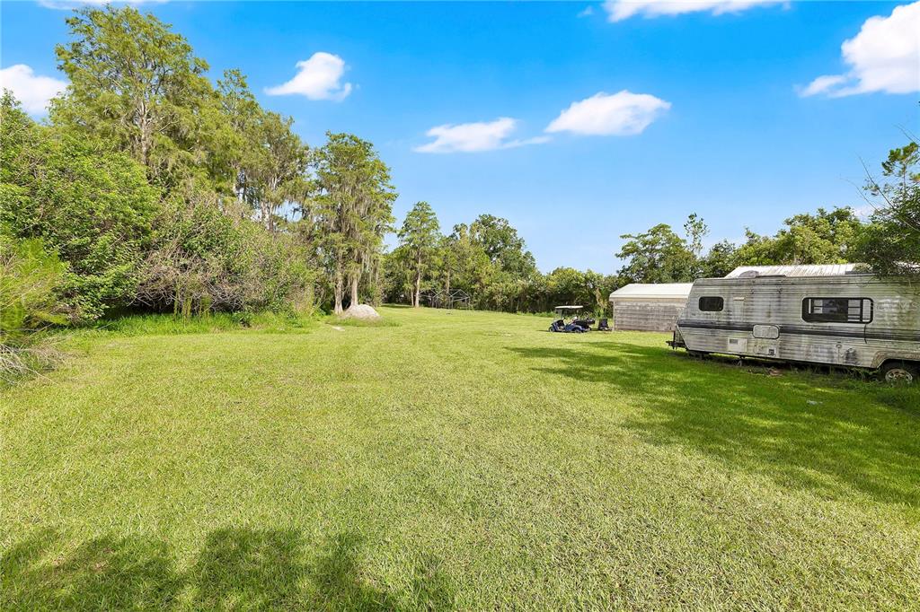 A grassy lot features a weathered travel trailer, a small shed, and mature trees — 3925 KAISER AVENUE, ST CLOUD, FL