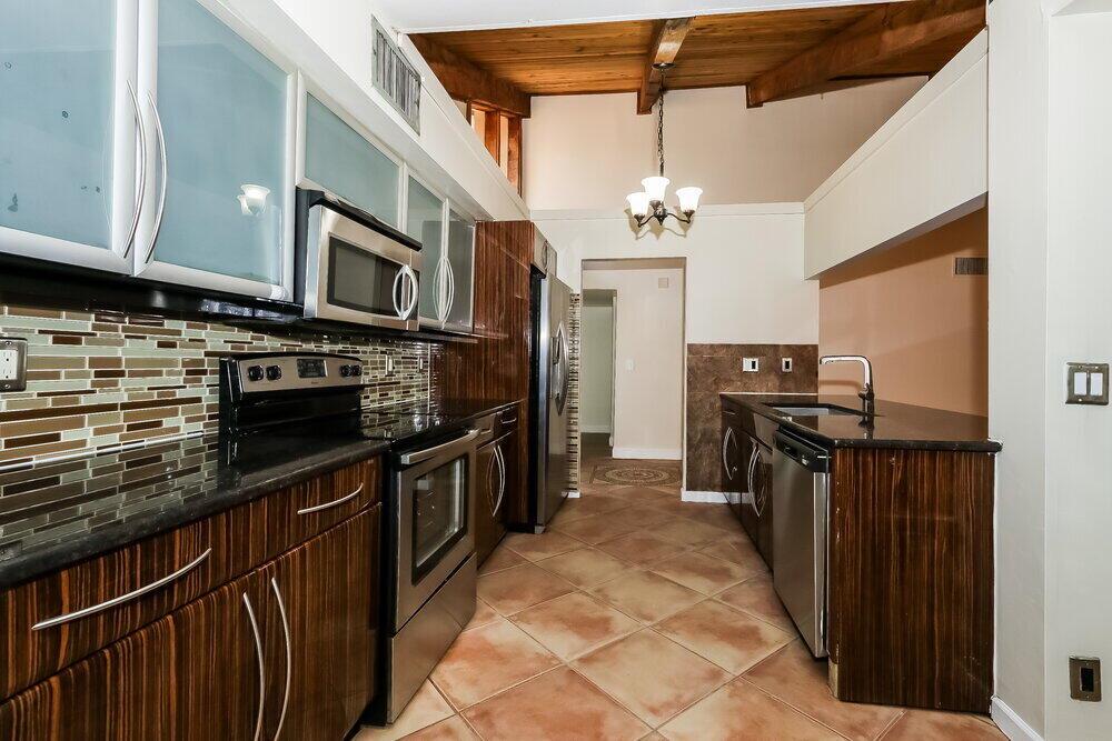 A galley kitchen features dark wood cabinets, granite countertops, stainless steel appliances, and tile flooring — BOCA RATON, FL