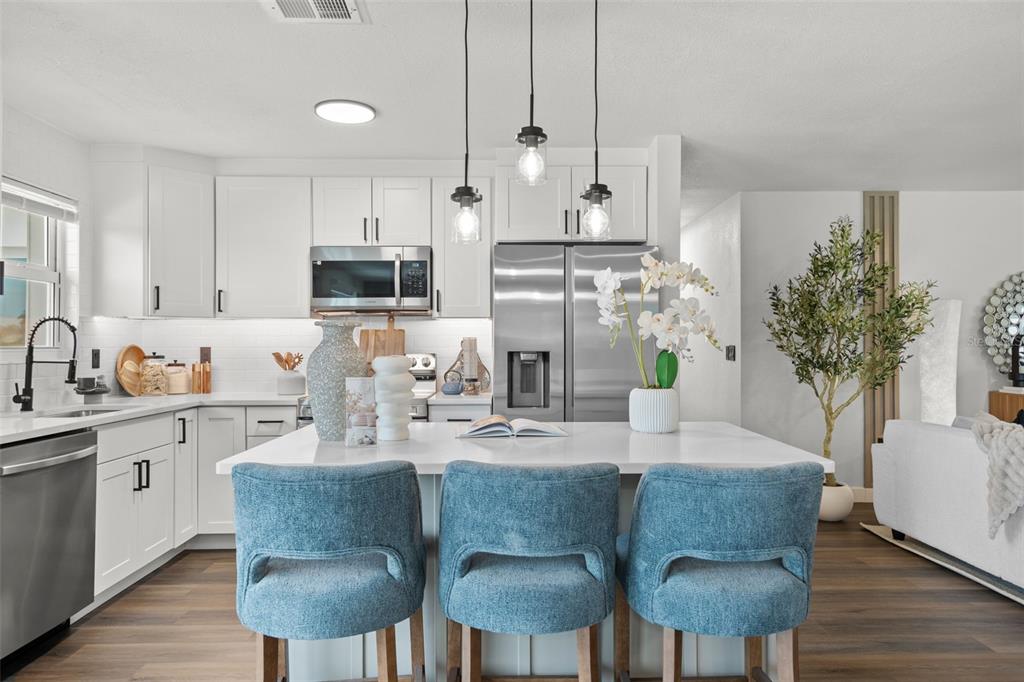 A modern kitchen features white cabinets, stainless steel appliances, a center island, and blue stools — 30 OAKLAND HILLS COURT, ROTONDA WEST, FL