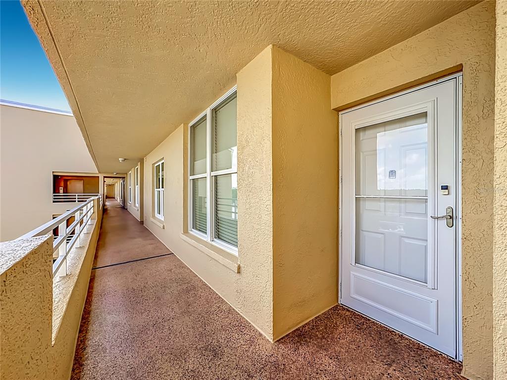 An exterior walkway features a white storm door, large windows, and a textured beige wall — 3740 PINEBROOK CIRCLE UNIT 607, BRADENTON, FL