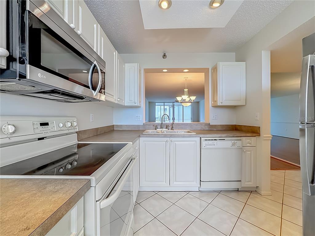 A kitchen features white cabinets, a glass-top stove, a microwave, and a pass-through window — 3740 PINEBROOK CIRCLE UNIT 607, BRADENTON, FL