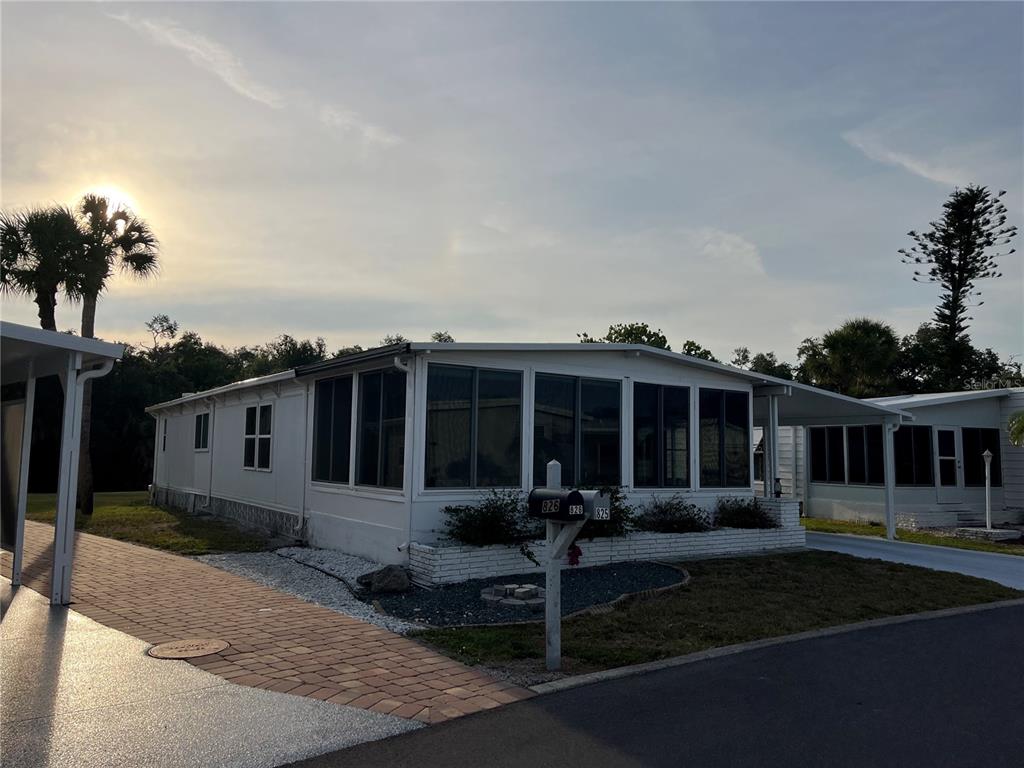 A white mobile home with a screened-in porch and a carport sits on a paved lot — 825 JOLANDA CIRCLE, VENICE, FL