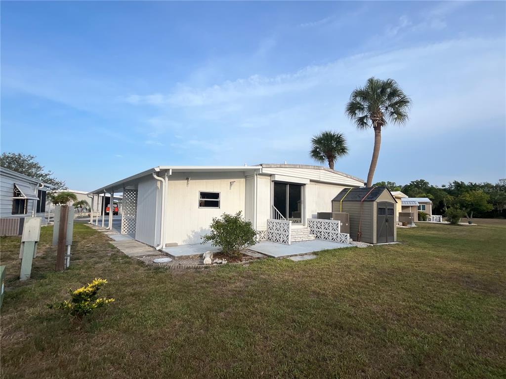 A single-story manufactured home with a side carport, a small shed, and palm trees — 825 JOLANDA CIRCLE, VENICE, FL
