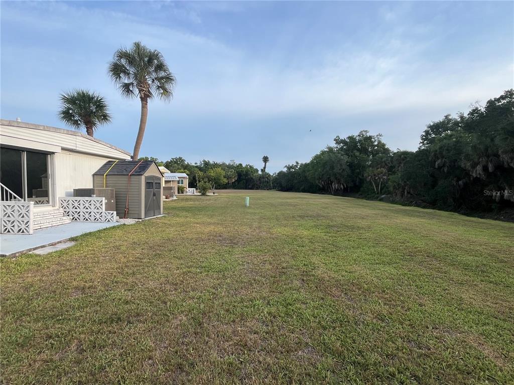 A grassy backyard extends from a mobile home toward a line of trees — 825 JOLANDA CIRCLE, VENICE, FL