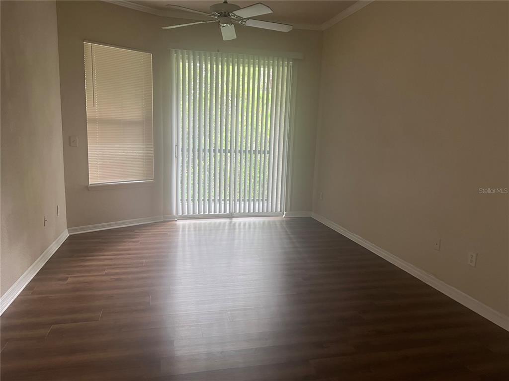 An empty room features wood-look flooring, a ceiling fan, a window with blinds, and sliding doors — 18107 PEREGRINES PERCH PLACE UNIT 6310, LUTZ, FL
