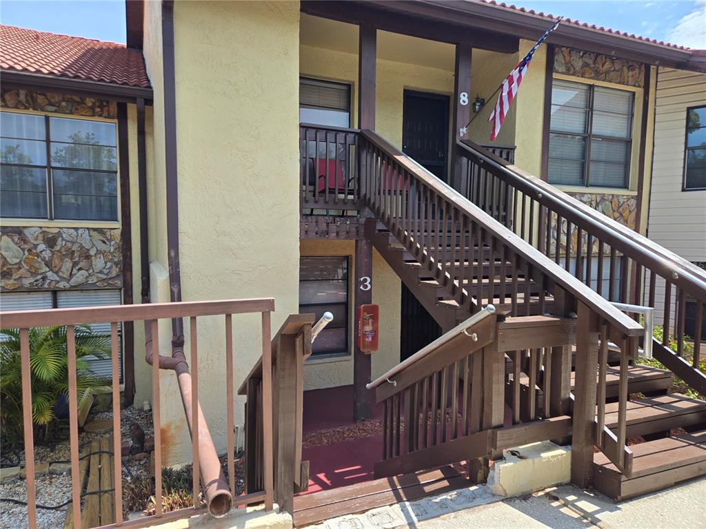 An exterior view of a two-story building with wooden stairs leading to an upper unit — 7741 FOREST TRAIL UNIT 3, PORT RICHEY, FL
