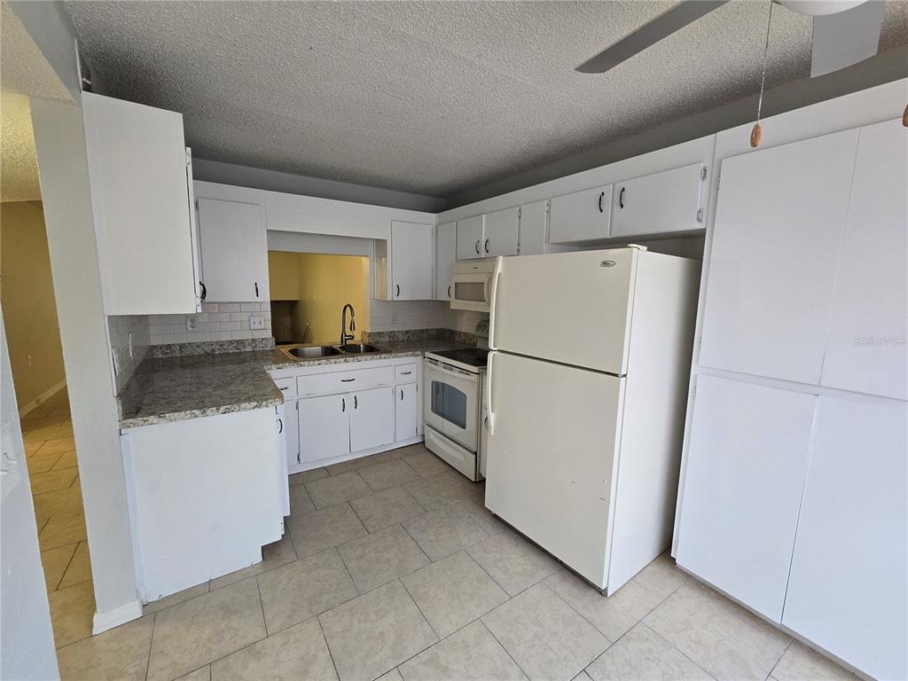 A kitchen features white cabinets, granite countertops, white appliances, and light-colored tile flooring — 7741 FOREST TRAIL UNIT 3, PORT RICHEY, FL