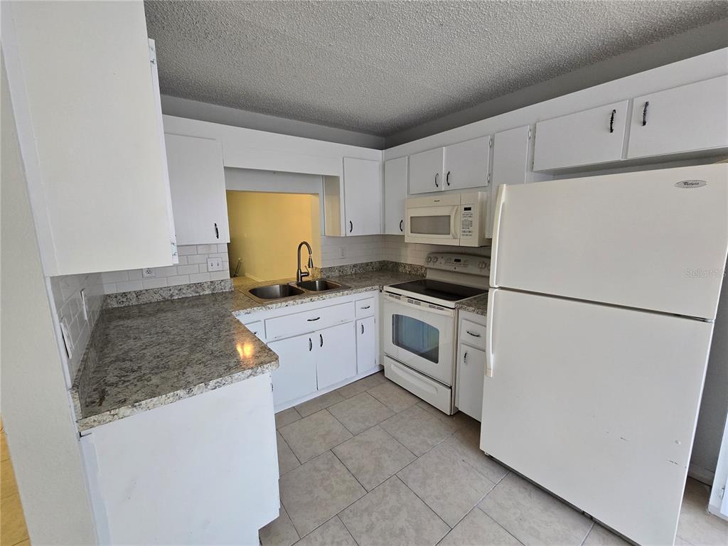 A kitchen features white cabinets, granite countertops, a white refrigerator, and a tiled floor — 7741 FOREST TRAIL UNIT 3, PORT RICHEY, FL